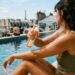 Une main féminine vaporise le spray solaire Avène Invisible SPF50 sur une peau bronzée au bord d'une piscine, flacon bien