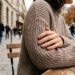 Une main aux ongles satinés beige-rosé posée sur un pull en laine côtelée, lumière naturelle d'automne